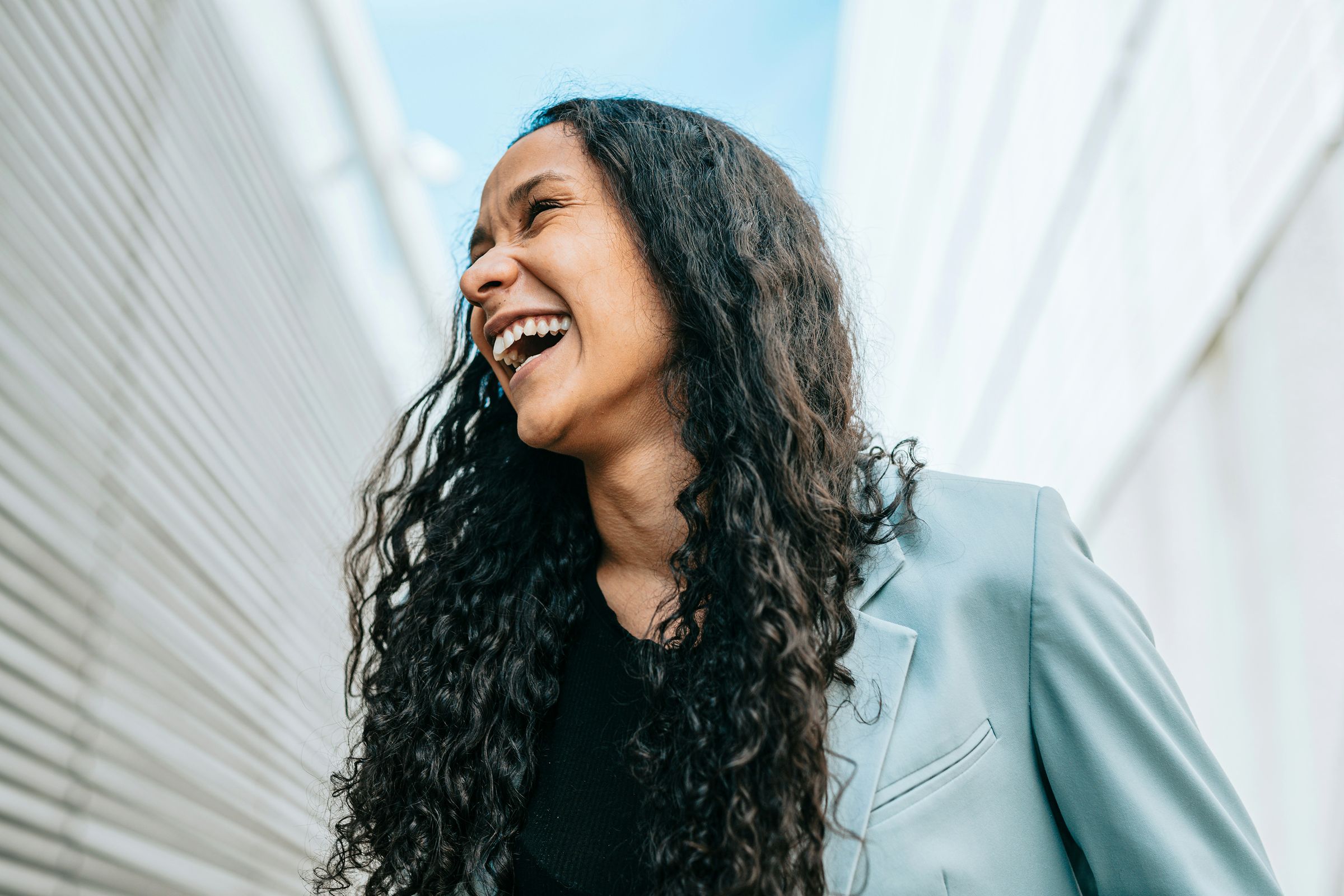 A woman laughing outdoors in a light blue blazer